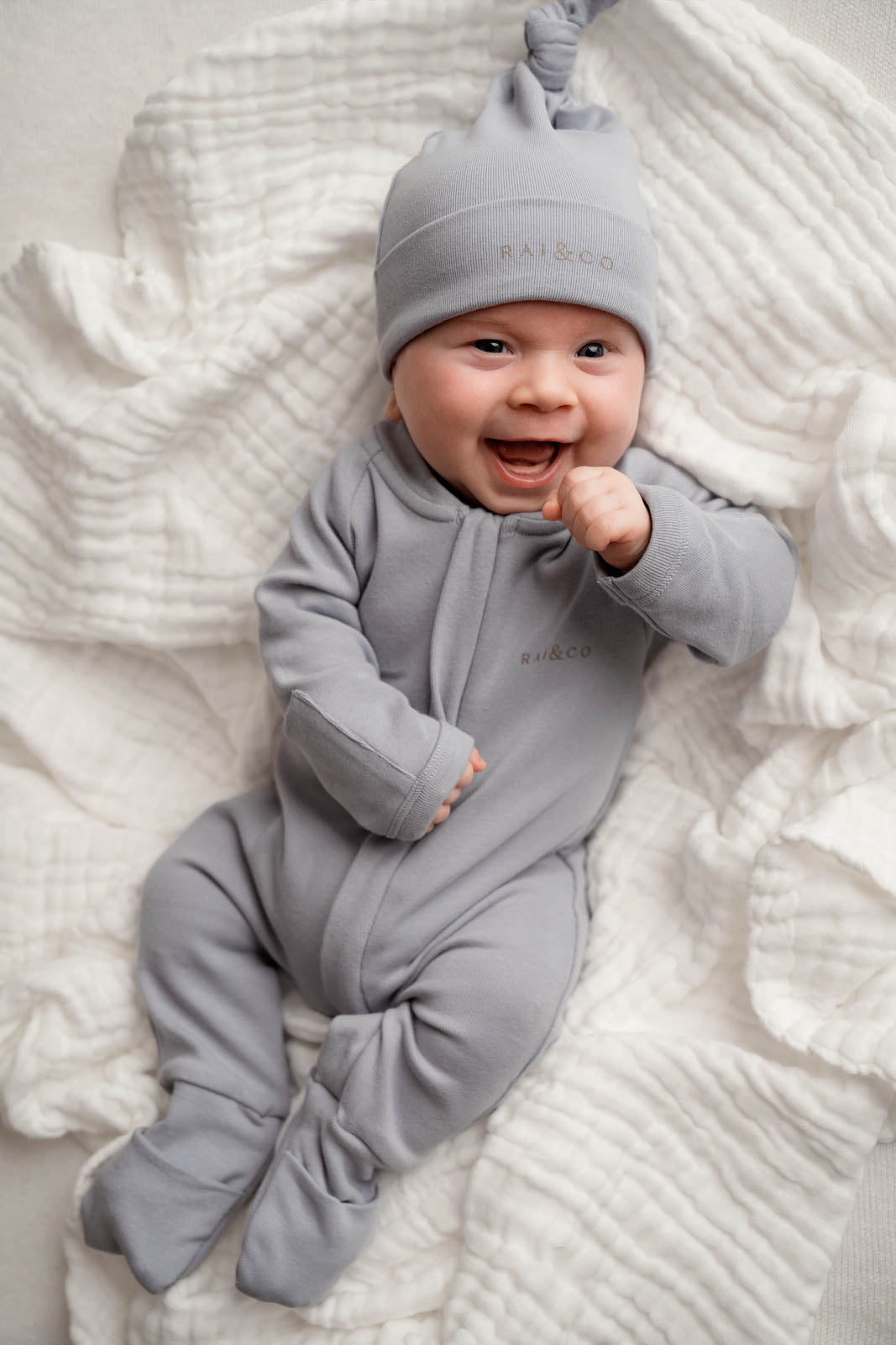 Baby lying on a white background, wearing the Baby Beanie Apple Knotted in Sky Blue.