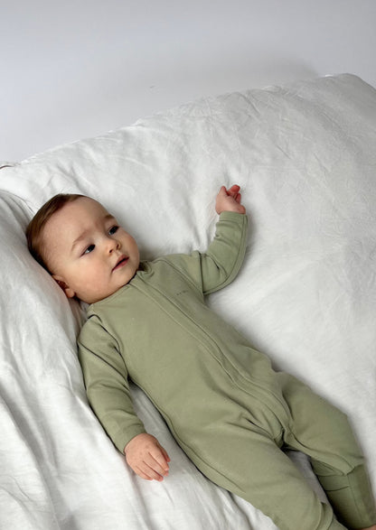 Baby wearing a Apple Onesie in Olive Green on a white bed 