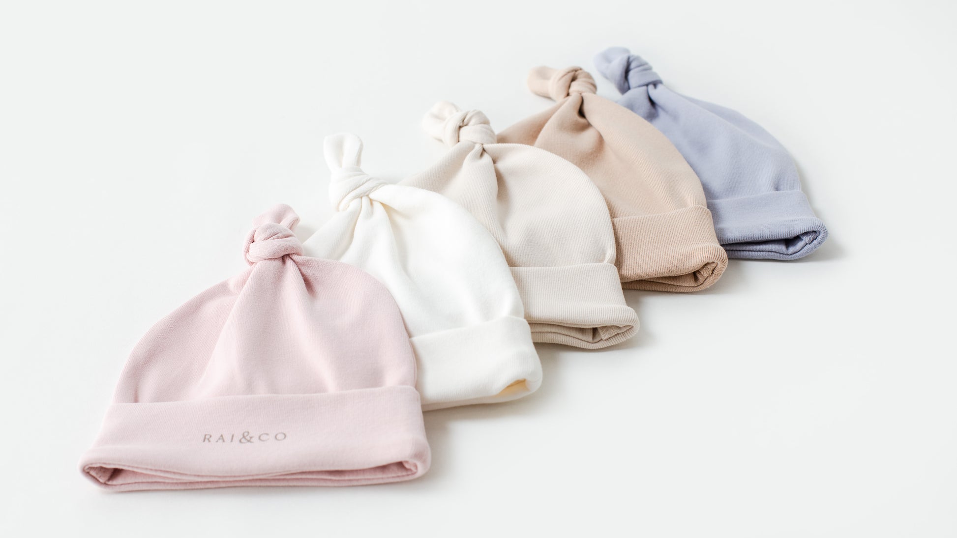 A collection of Baby Beanie Apple Knotted in Available Colours displayed in a row with the brand name visible on the bottom right beanie.
