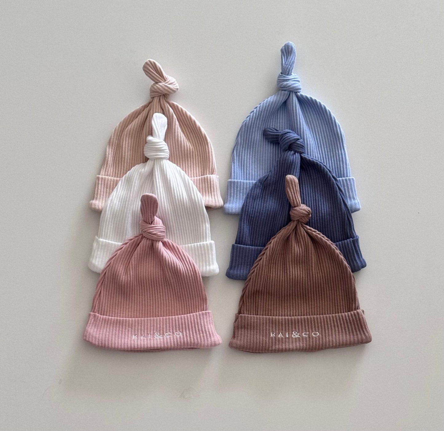 six Baby Beanie Ribbed Knotted  in available colours on a light background