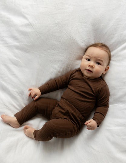 Baby wearing a Basic Leggings in Chocolate on a white bed
