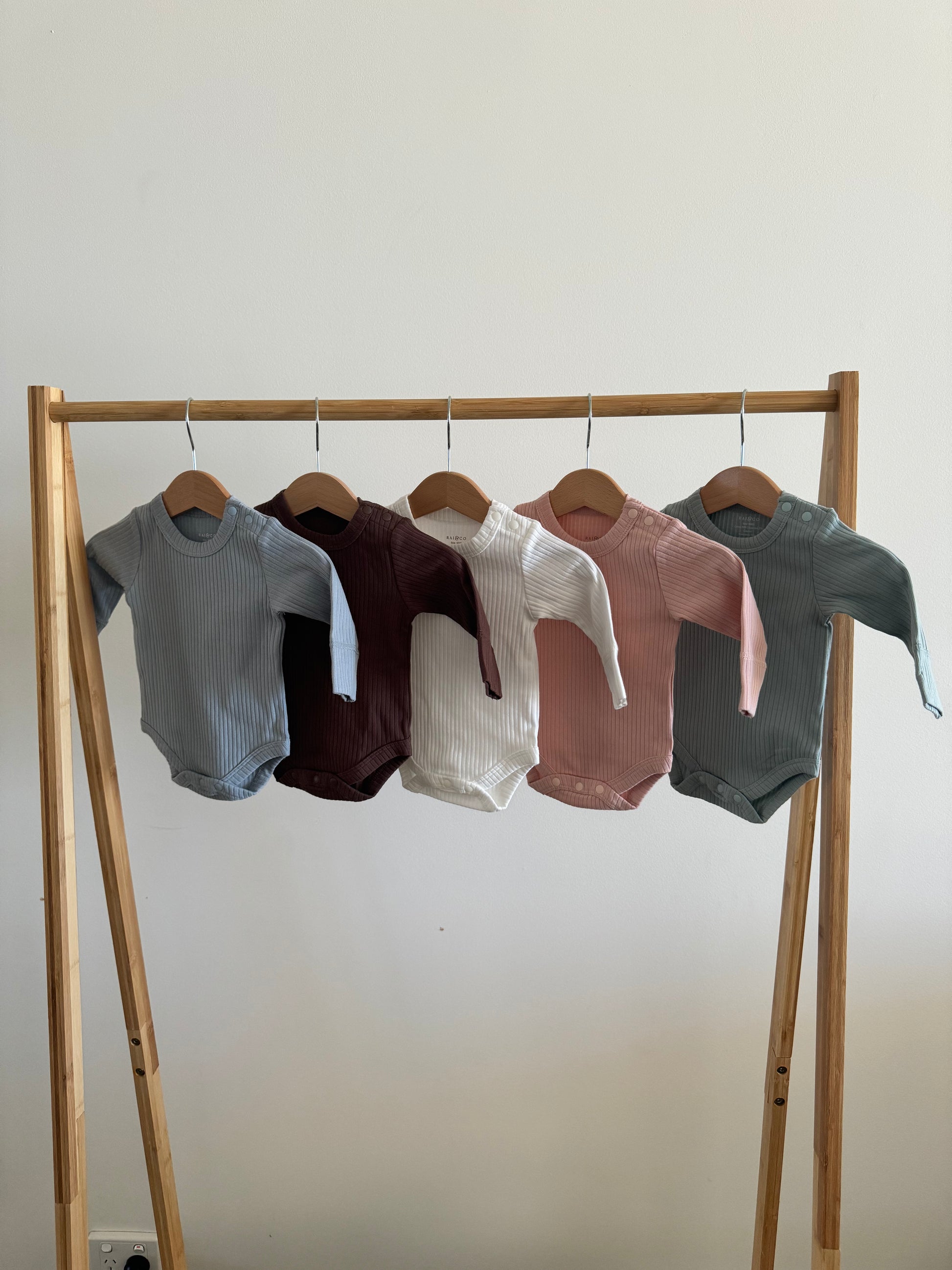 Set of Basic Longsleeve Bodysuit Bundle Available Colours on a wooden rack against a white wall 