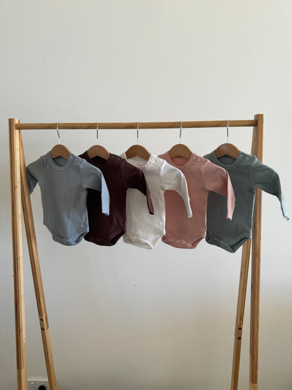 Set of Basic Longsleeve Bodysuit Bundle Available Colours on a wooden rack against a white wall 