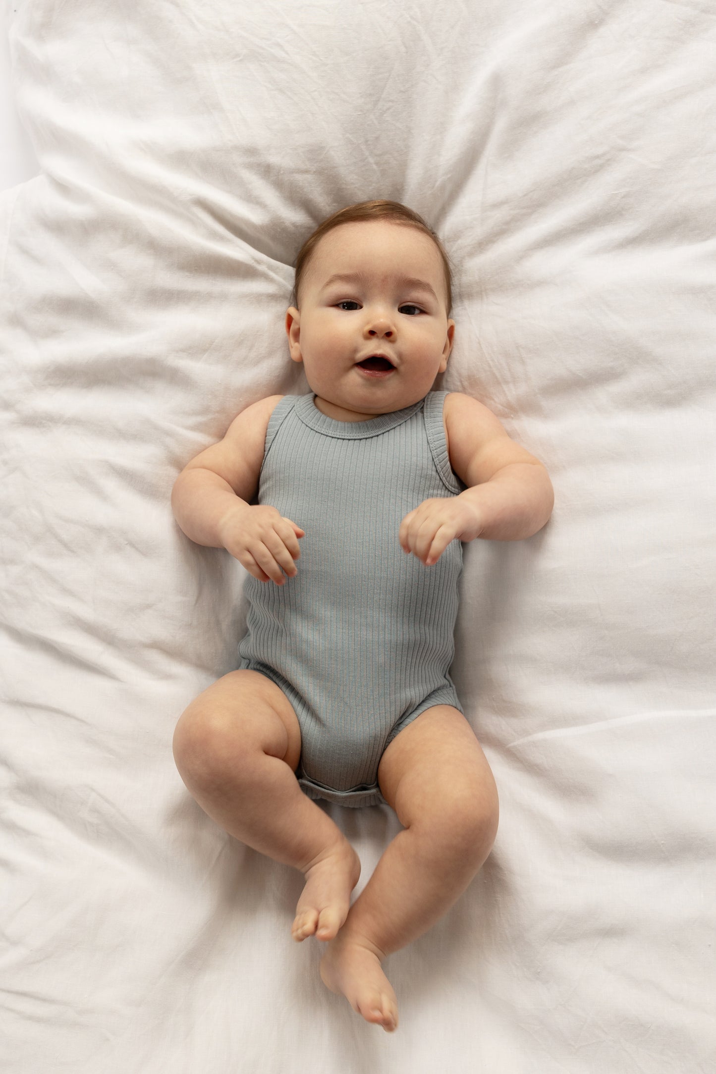 Baby wearing a Basic Singlet Bodysuit in Dusty Blue on a white bed