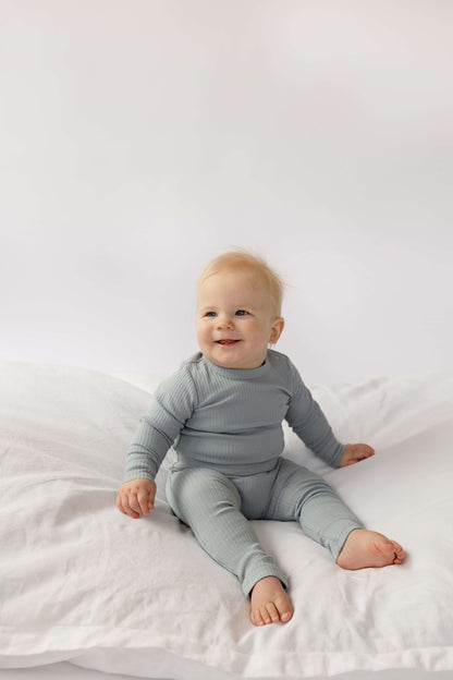 Baby in a Baby Boy Basic Longsleeve Bodysuit in Dusty Blue sitting on a white bed