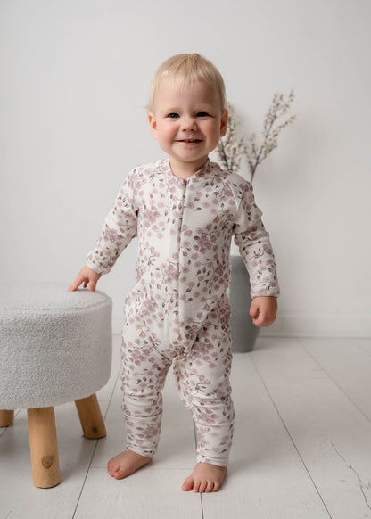 Child wearing a Bloom Floral Onesie Pink standing in a minimalistic room with a white background