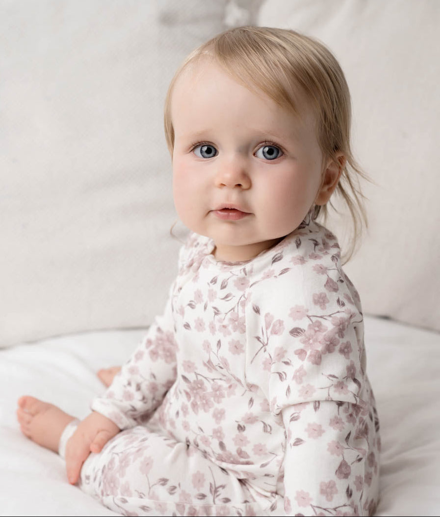 Baby in a Bloom Floral Onesie Pink sitting on a white couch