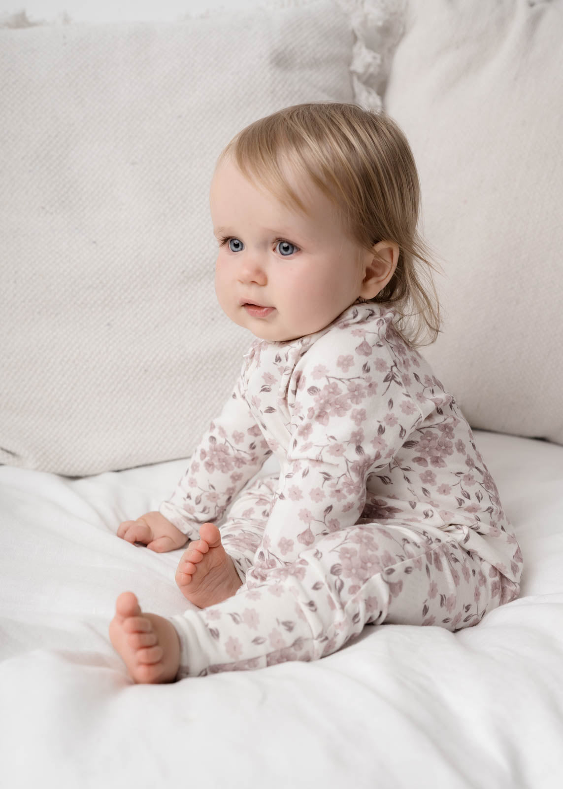 Baby in a Bloom Floral Onesie Pink sitting on a white bed