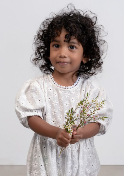 A young child wearing a Eliza Embroidered Romper in White with embroidered details, featuring puffed shoulders and a soft neckline.