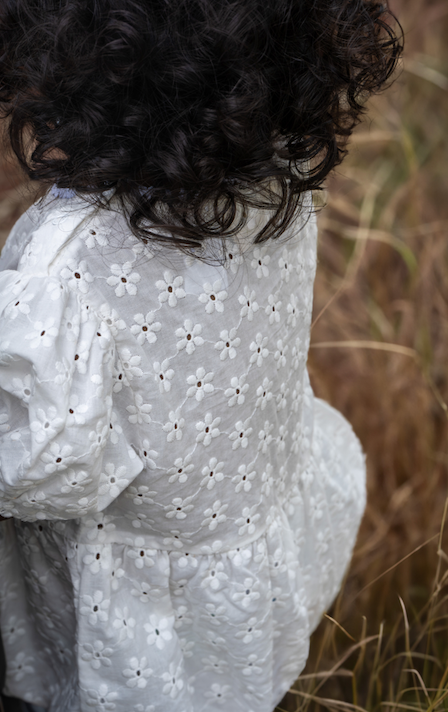 A baby wearing the Eliza Embroidered Romper in White on a grassy background.