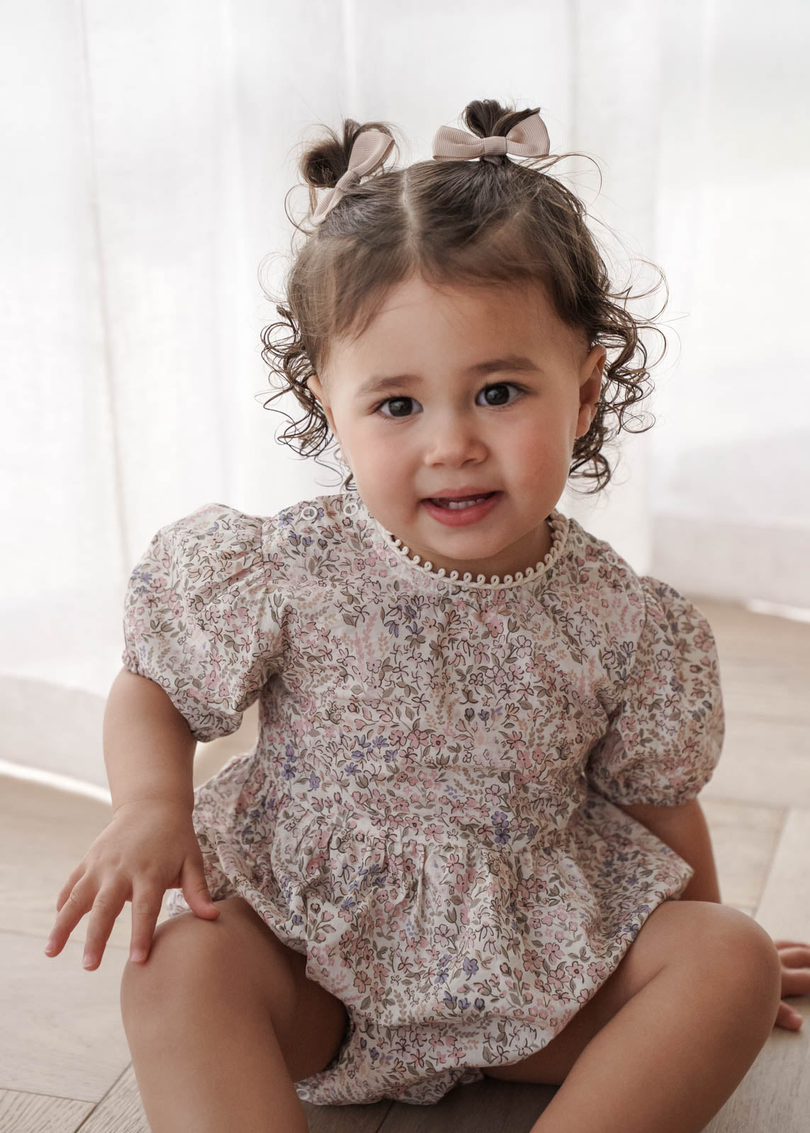 Child wearing a Eliza Floral in Cream sitting on a light wooden floor.