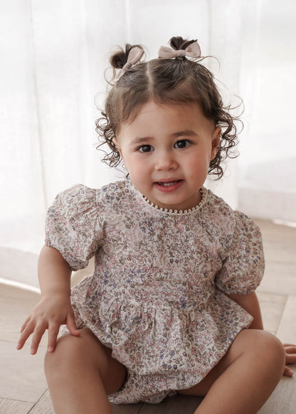 Child wearing a Eliza Floral in Cream sitting on a light wooden floor.