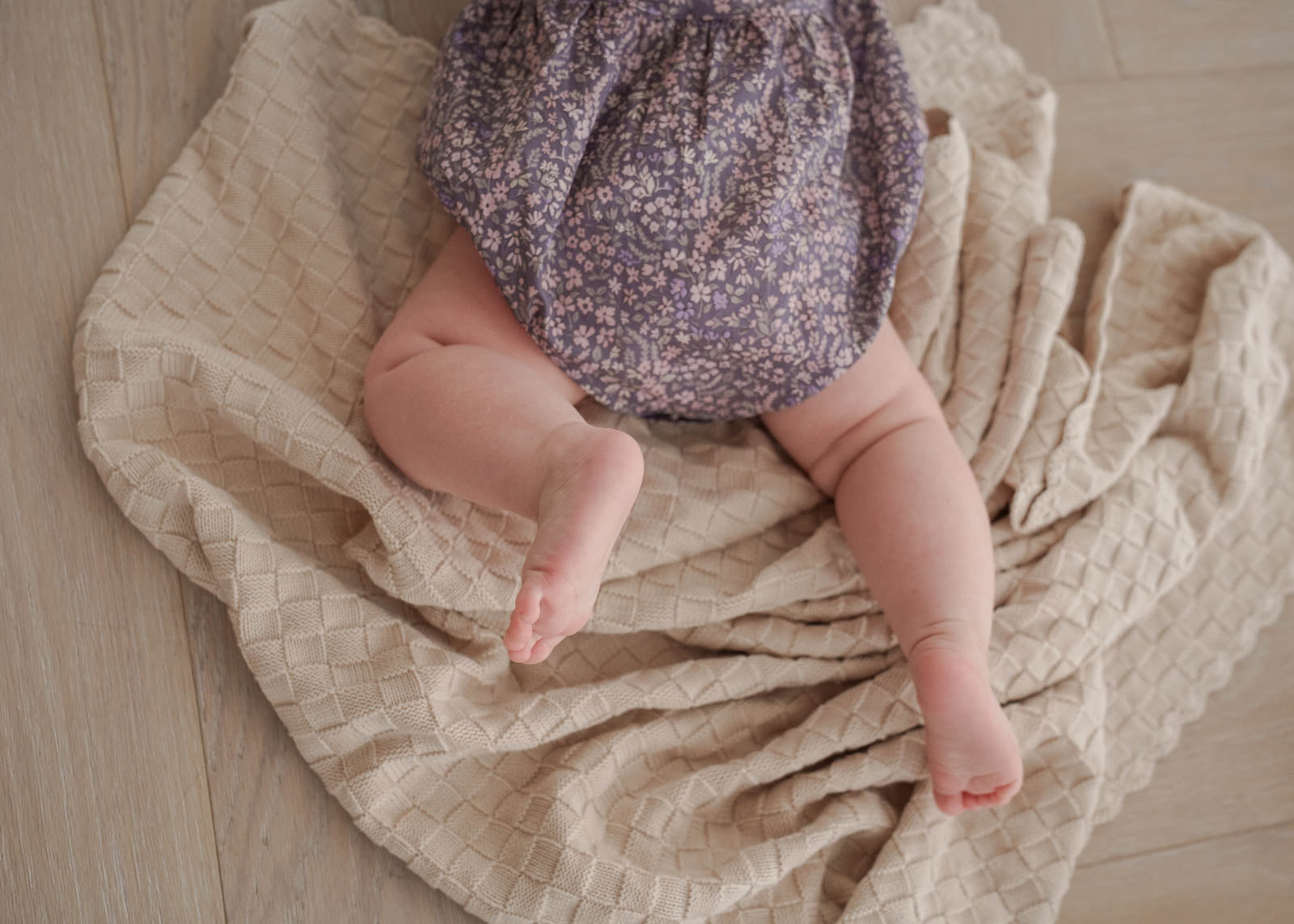 Baby in Eliza Floral Romper in Indigo lying on a textured beige blanket
