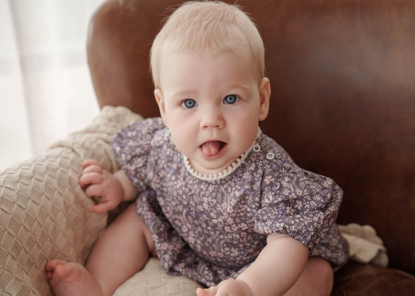 Baby wearing a Eliza Floral Romper in Indigo sitting on a couch