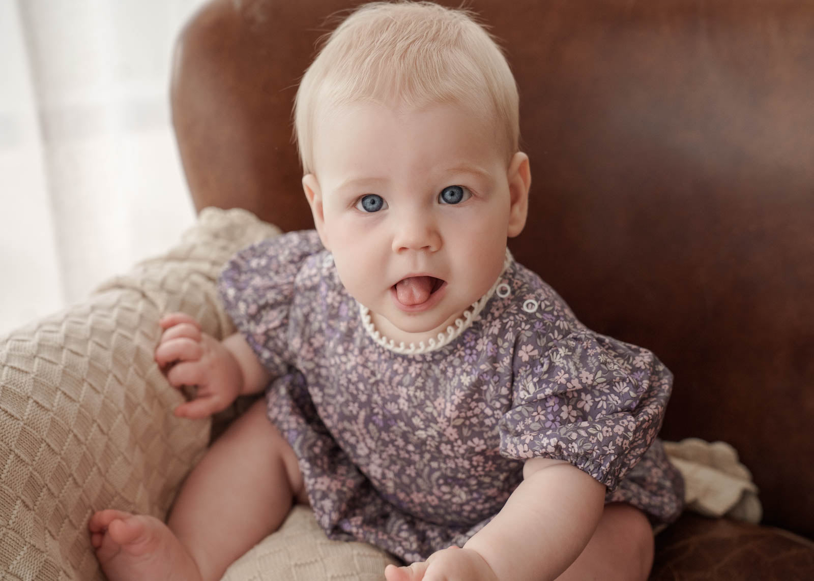 Baby wearing a Eliza Floral Romper in Indigo sitting on a couch