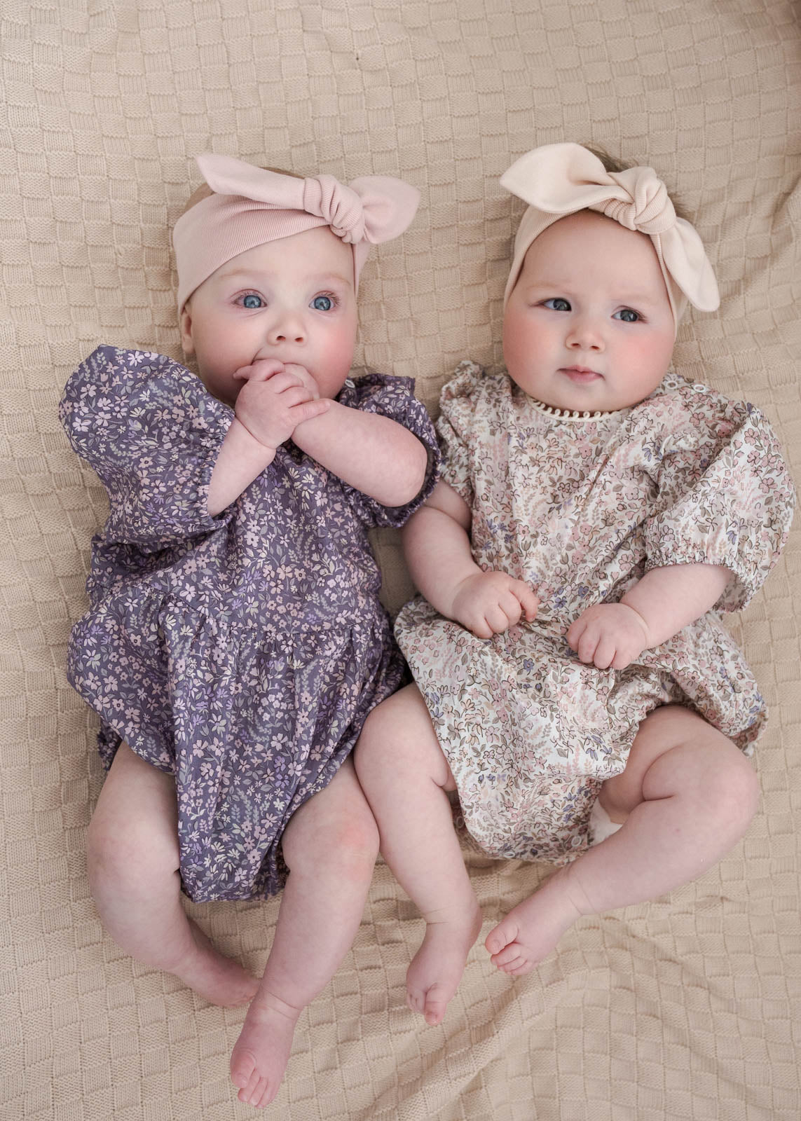 Two babies in Eliza Floral in Romper Indigo and Cream lying on a beige surface
