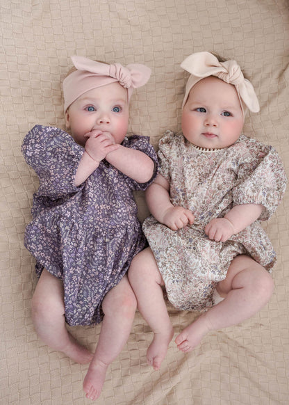 Two babies in Eliza Floral in Romper Indigo and Cream lying on a beige surface