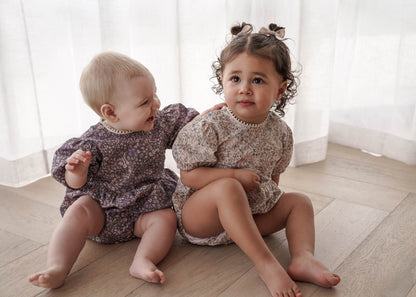 Two young children in Eliza Floral Romper in  Indigo and Cream sitting on a wooden floor.