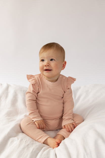 A baby wearing a Frill Basic Long Sleeve Bodysuit in Beige sitting on a light background.