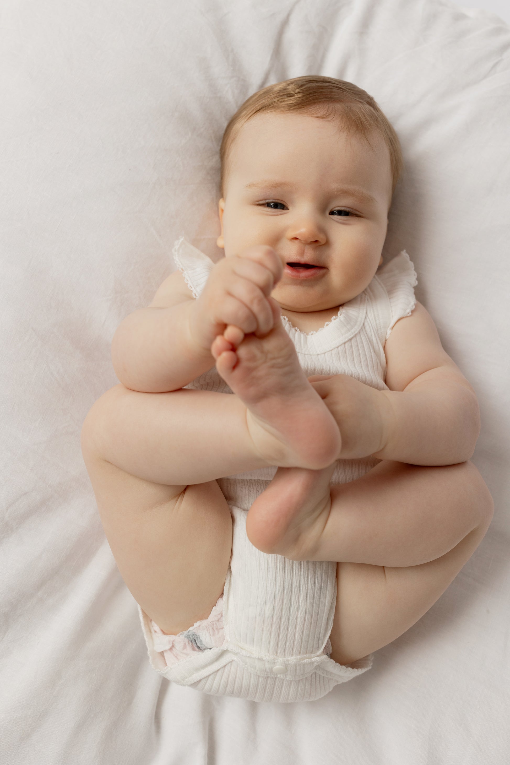 Baby wearing a Frill Basic Singlet Bodysuit in White on a white bed