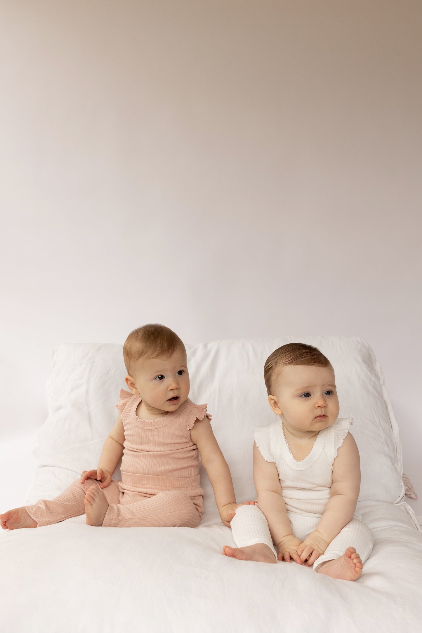 Two babies sitting on a white surface, wearing Frill Basic Singlet Bodysuit in White and Beige 
