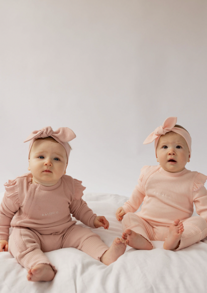 two babies wearing a Frill Ribbed Onesie in Powder Pink and Light Pink on a white background 