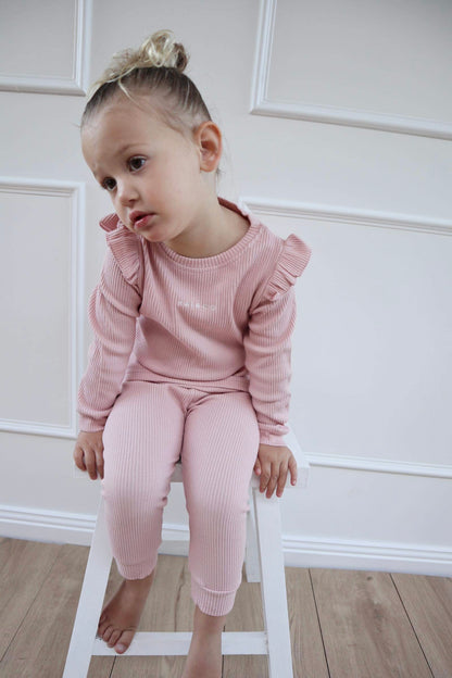 A toddler in wearing Frill Ribbed Two Piece in Powder Pink, sitting against a white background.