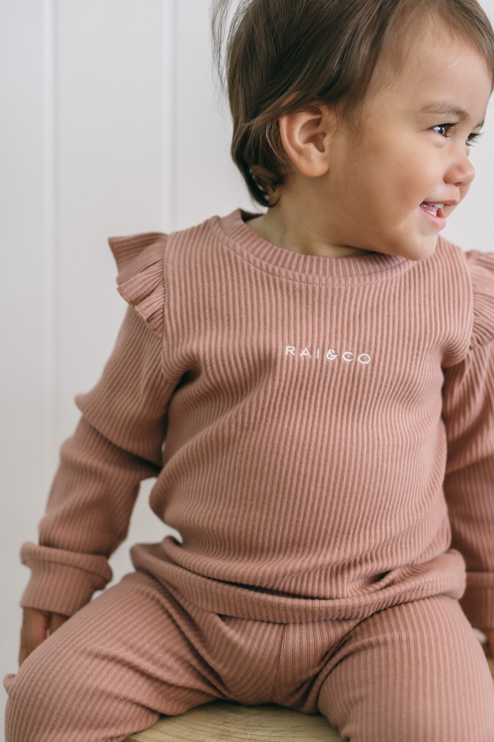 Child wearing a Frill Ribbed Two Piece in Powder Pink, sitting on a white surface.