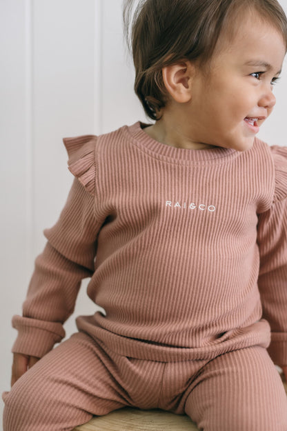Child wearing a Frill Ribbed Two Piece in Powder Pink, sitting on a white surface.