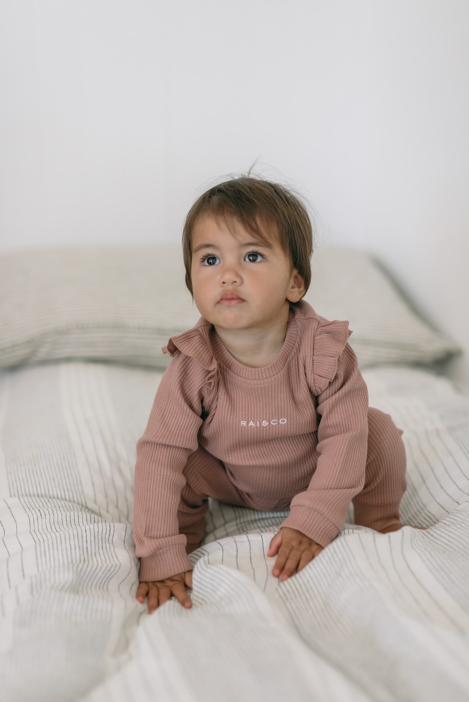 Baby wearing a Frill Ribbed Two Piece in Powder Pink on a white bed