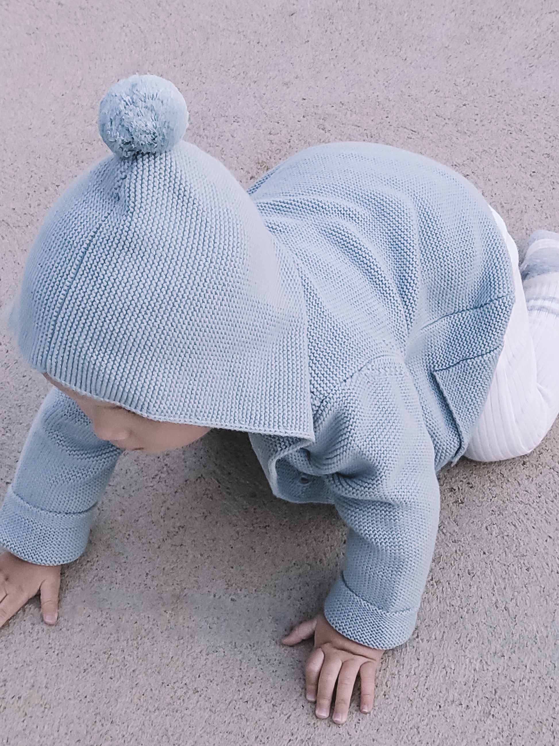 A baby wearing the Hooded Knit in Blue, crawling on the floor.