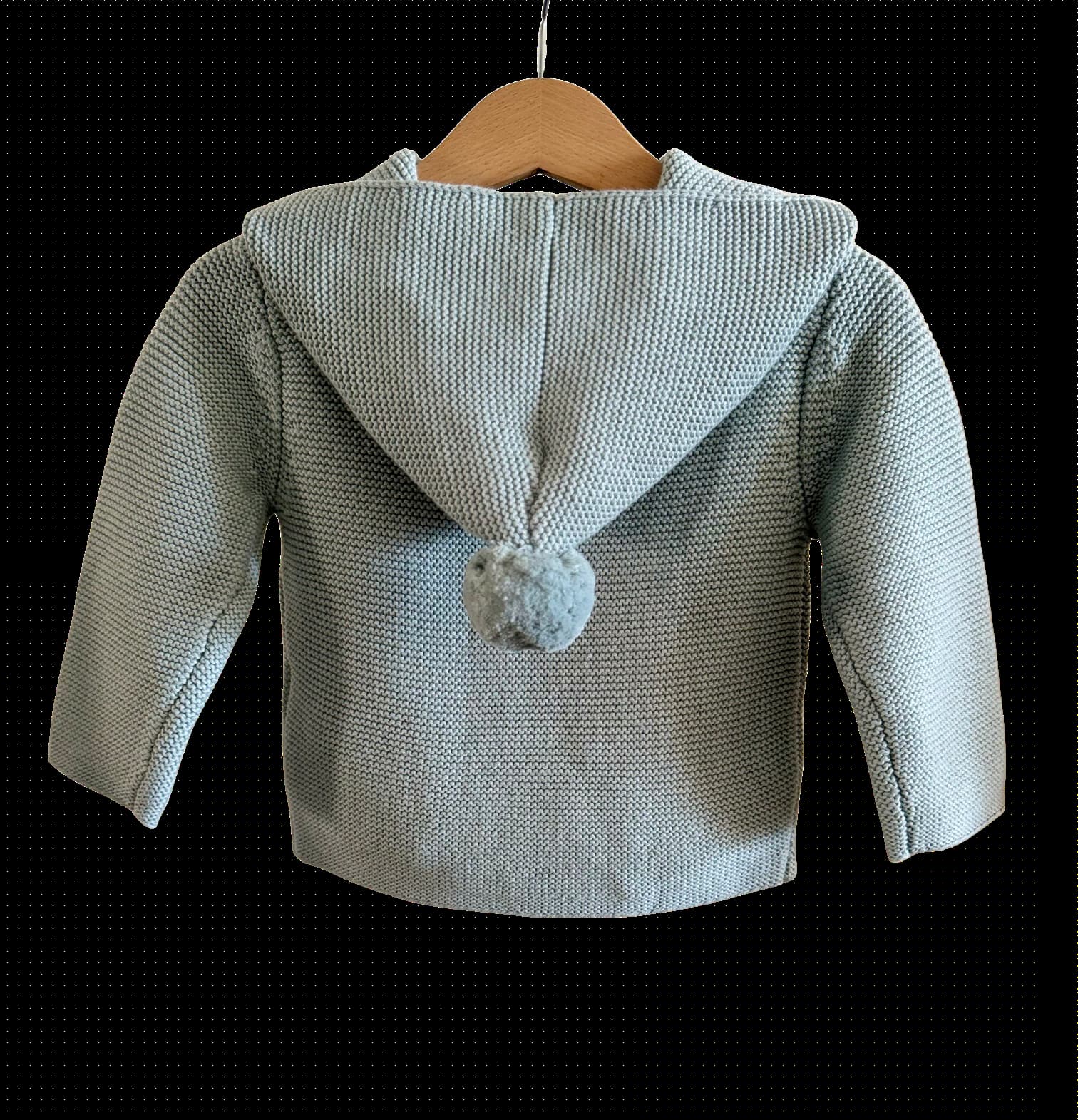 Hooded Knit in Blue in a wooden hanger against a black background