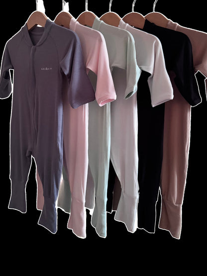Set of Lightweight Eco Onesie in Available Colours hanging on a rack against a black background.