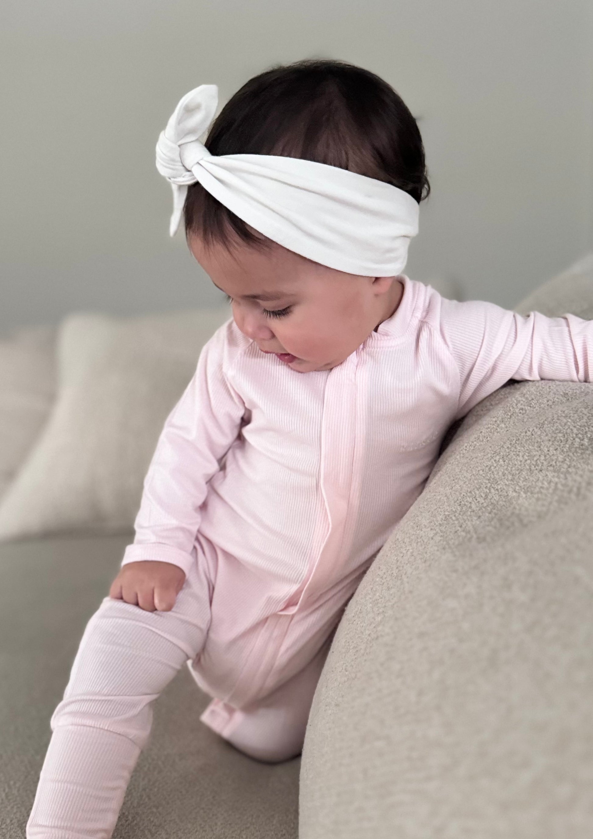 A baby wearing a Lightweight Eco Onesie in Pink with a bow on the head