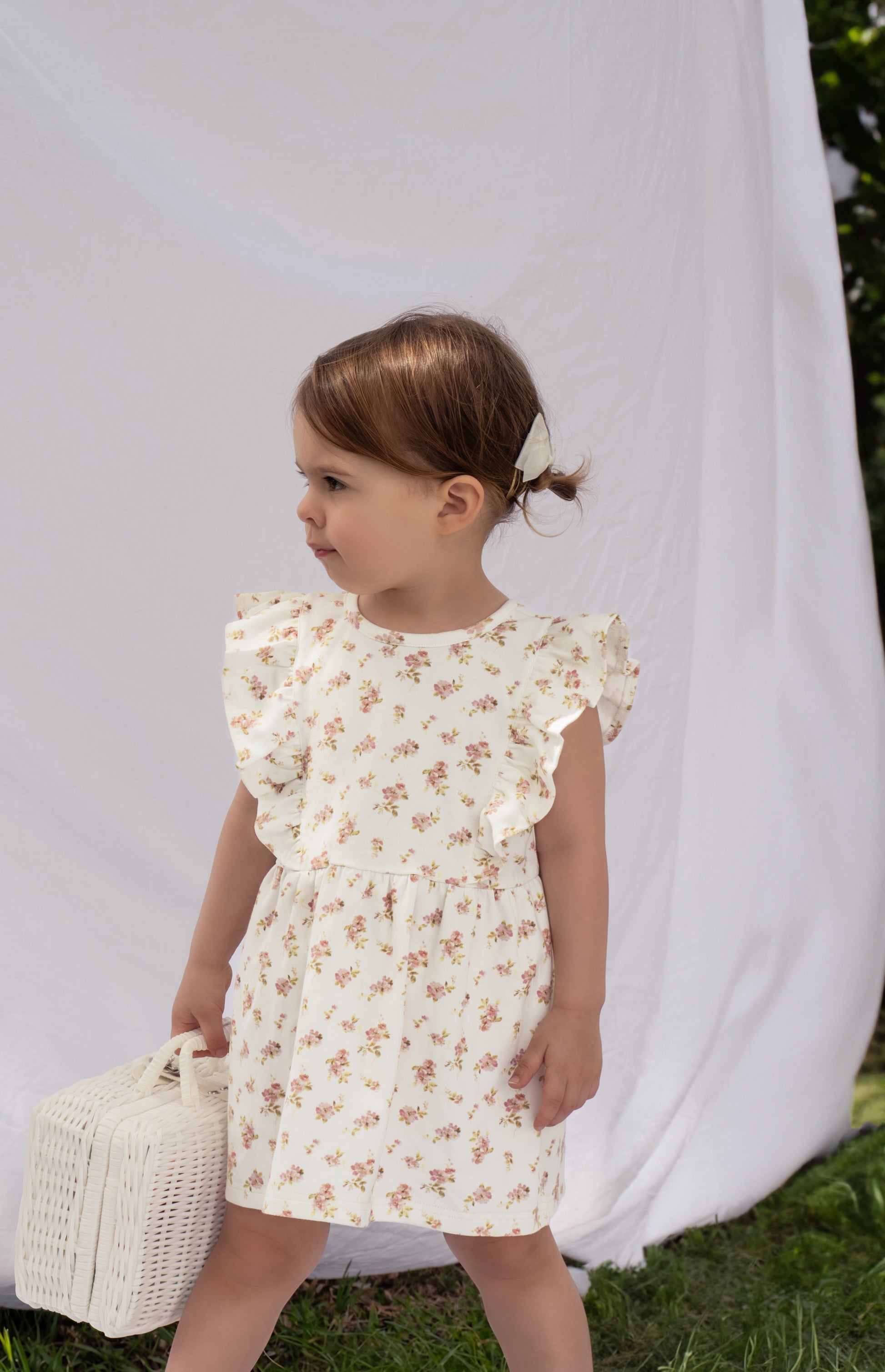 A young child wearing a Lottie Floral Dress With Pilchers in Pink Floral against a white backdrop.