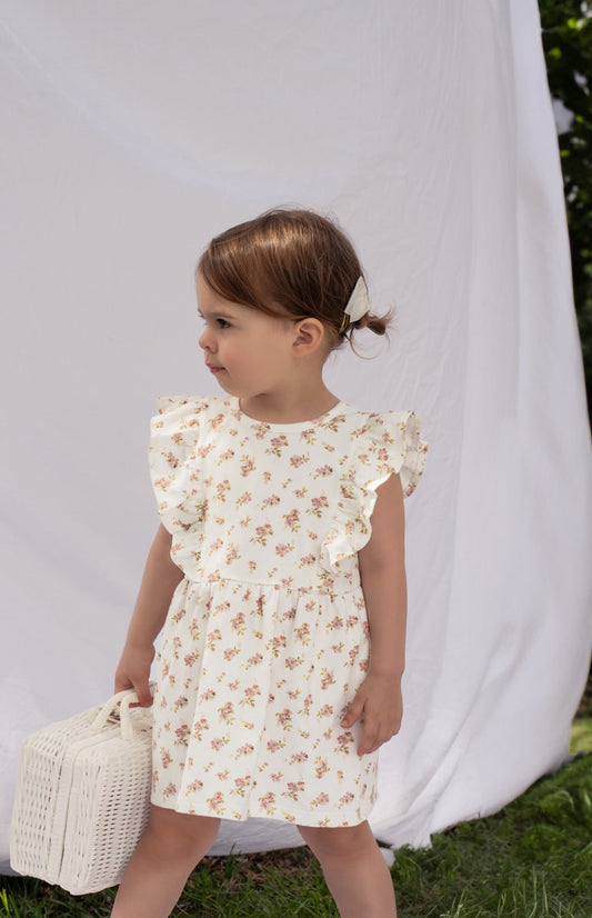 A young child wearing a Lottie Floral Dress With Pilchers in Pink Floral against a white backdrop.