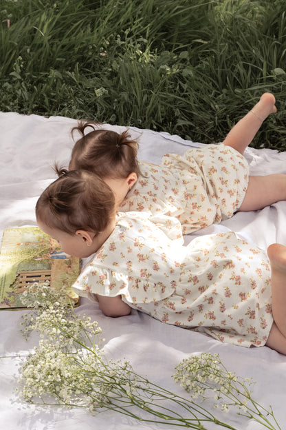 Two young children wearing the Lottie Floral Dress with Pilchers in Pink Floral, lying on a white mat.