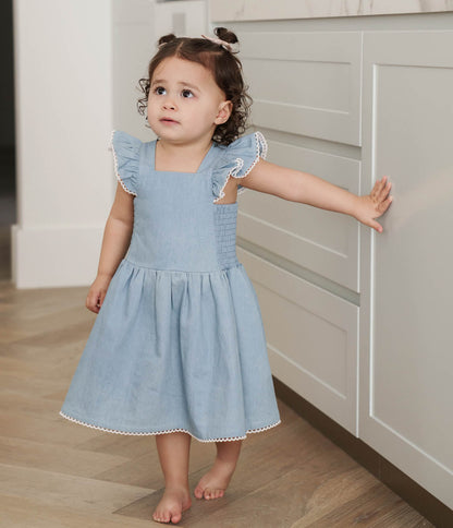 Young girl in a Denim Maddie Dress standing in a kitchen.