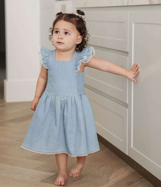 Young girl in a Denim Maddie Dress standing in a kitchen.