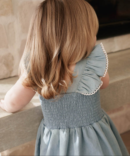 Child wearing a Maddie Dress in Denim standing on a stone floor.