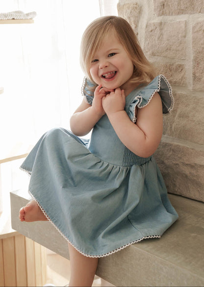 Child wearing a Maddie Dress in Denim sitting on a stone step.