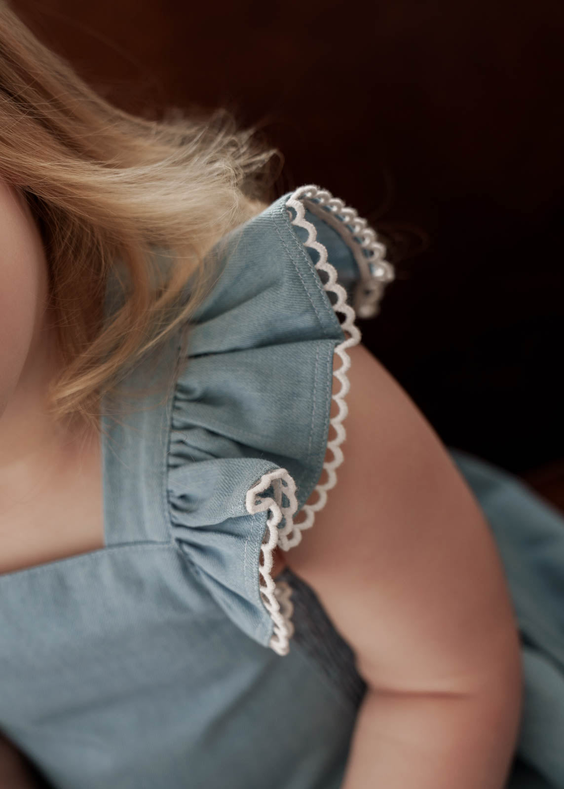 Close-up of a young girl wearing a Maddie Dress in Denim on a dark background