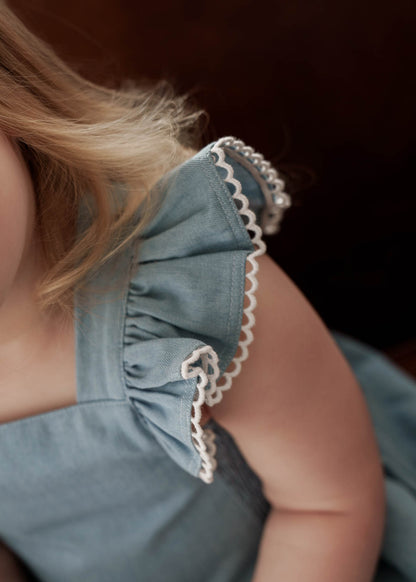 Close-up of a young girl wearing a Maddie Dress in Denim on a dark background