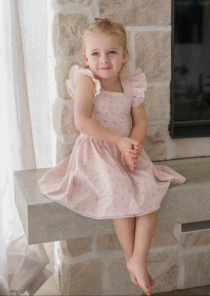 Young girl in a Pink Floral Maddie Dress sitting on a stone ledge.