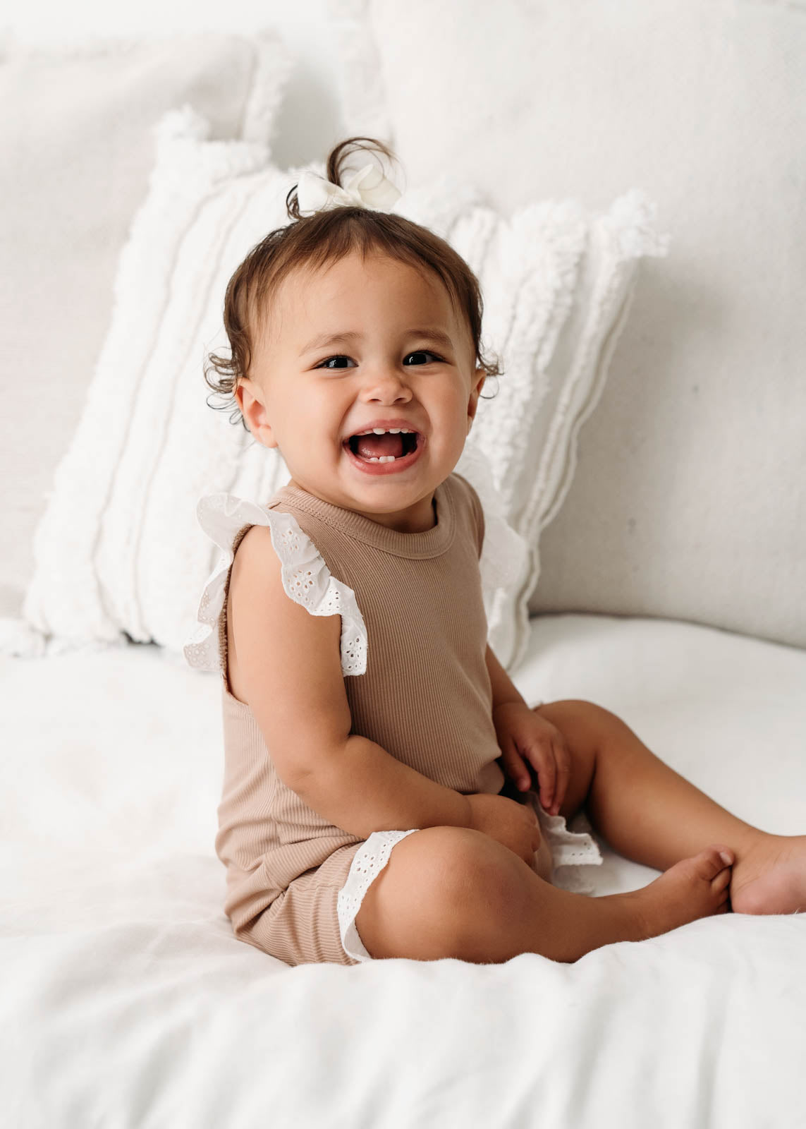 A smiling baby wearing a Mini Ribbed Lace Frill Romper in Beige