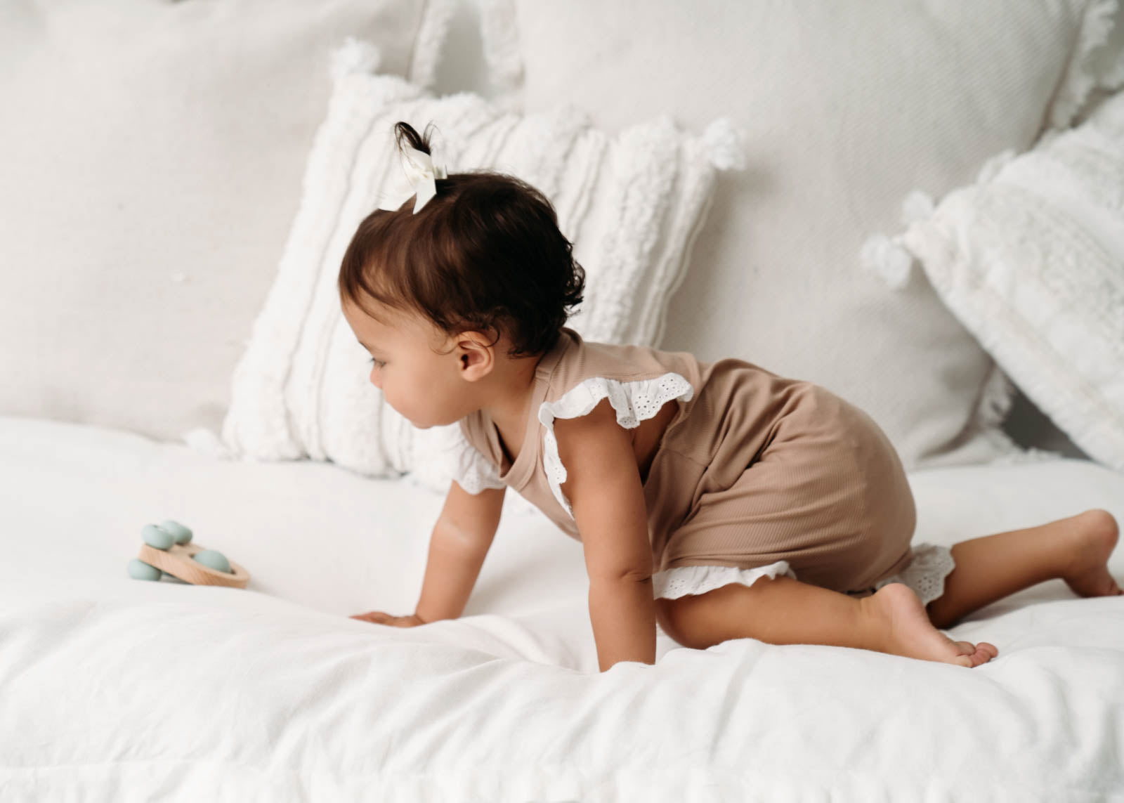 Baby wearing a Mini Ribbed Lace Frill Romper in Beige on a white bed 