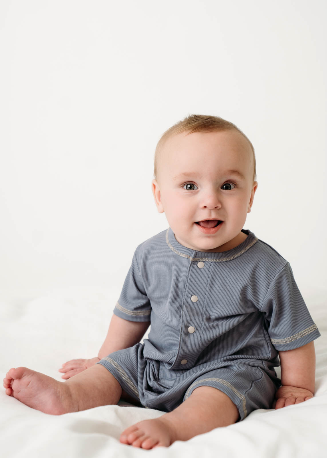 A sitting baby wearing a Mini Ribbed Romper in Royal Blue on a white background