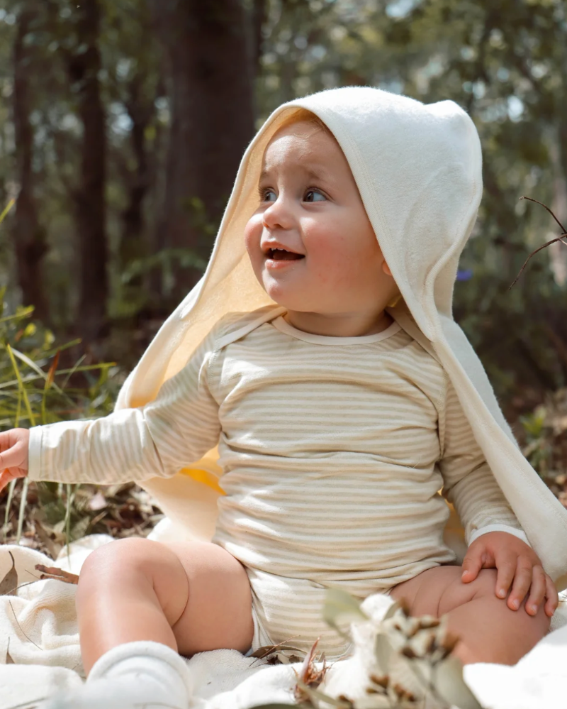 Baby wearing a Organic Baby Hooded Bath Towel in White sitting outdoors with trees in the background