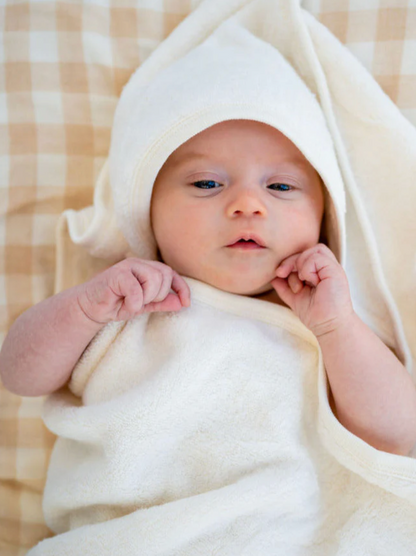 Baby wrapped in Organic Baby Hooded Bath Towel in White on a beige blanket
