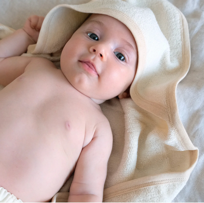Baby wrapped in Organic Baby Hooded Bath Towel in White on a soft surface